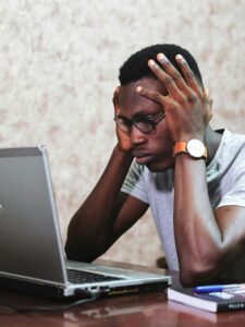 A man appears frustrated while working on a laptop in an office setting, showcasing remote work challenges.