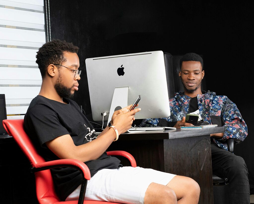 Two young men engaged with smartphones at a modern office desk in Port Harcourt.